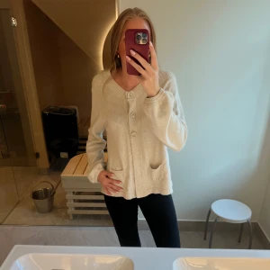 Beige kofta med knappar - Mysig beige kofta från KappAhl med ribbade detaljer upptill, stora knappar framtill och två fickor. Långärmad och i mjukt stickat material