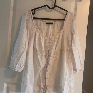 Vit randig blus från Vero Moda - Luftig vit blus från Vero Moda med tunna ljusa ränder. Modellen har trekvartsärmar, knappar framtill och en lös passform med söt urringning. Perfekt för en chill och avslappnad stil.