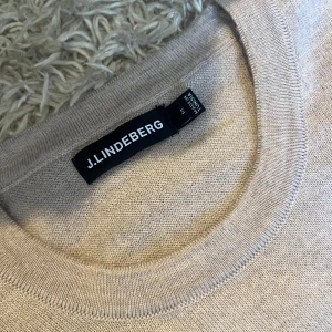 Beige stickad tröja från J.Lindeberg - Snygg beige stickad tröja från J.Lindeberg med diskret JL-logo broderad på bröstet. Tröjan har rund halsringning, långa ärmar och ribbade muddar. Nytt skick utan anmärkningar, använd ca 2 gånger. Storlek M men mått kan såklart skickas vid osäkerhet. Postas antigen samma dag som köp eller dagen därpå🙌💯