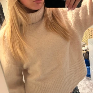 Beige stickad polotröja - Mysig beige stickad polotröja med bred krage och lång ärm. Tröjan har en loose passform och ribbade muddar vid ärmslut och nederkant. Perfekt för lager-på-lager och chill dagar.