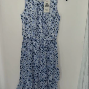 Blommig blå sommarklänning  - Söt ärmlös klänning från Hampton Republic med blått blommönster på vit botten. Klänningen har resår i midjan och volang nertill, perfekt för varma dagar. Lätt och luftig känsla, passar dig som gillar en feminin och fräsch stil. Aldrig använd , lappar kvar. Nypris 299 kr