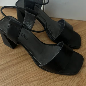 Vintage! Svarta klackskor från Tizzano - Snygga svarta klackskor från Tizzano med öppen tå och breda remmar. Skorna har en stabil blockklack och en elegant design som passar perfekt för festliga tillfällen.