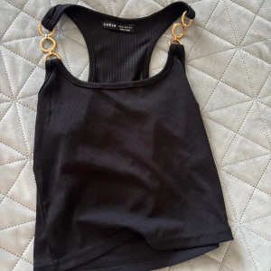 Svart ribbad linnetopp från Shein - Snygg svart ribbad linnetopp från Shein med guldfärgade ringdetaljer vid axelbanden. Perfekt för en stilren look. 🖤