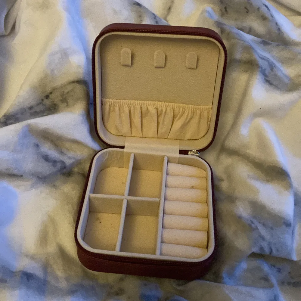 Praktiskt rött smyckeskrin med flera fack för organisering av smycken. Insidan är klädd i mjukt material för att skydda dina smycken. Perfekt för att hålla ordning på ringar, halsband och örhängen.. Asusteet.