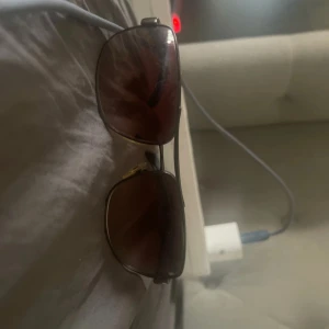 Solglasögon från Prada - Snygga solglasögon från Prada med bruna glas och en elegant metallram. Skalmarna har en röd detalj med Prada-loggan. Perfekta för en stilren look.