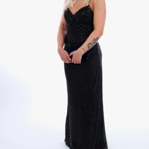 Svart glittrig långklänning/ balklänning - Elegant svart glittrig långklänning med smala axelband och snörning i ryggen. Perfekt för en glamorös kväll på röda mattan. Klänningen har en figurnära passform. Använd 1 gång på balen 2024. Stl 36. Är uppsydd nudda marken perfekt med klackar som är ca 5 cm. Längd på personen är 1.58. Klänningen är Köpt L&S i Göteborg  