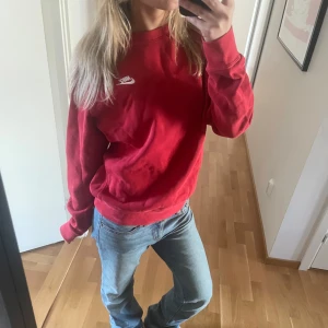 Röd sweatshirt från Nike - Säljer en röd sweatshirt från Nike med deras klassiska logga på bröstet. Tröjan har långa ärmar och en avslappnad passform, perfekt för en casual look. Den har några defekter framtill som syns på andra bilden men förutom det är den i bra skick☺️Den är i storlek Xs men skulle säga att den sitter som en S/M. 