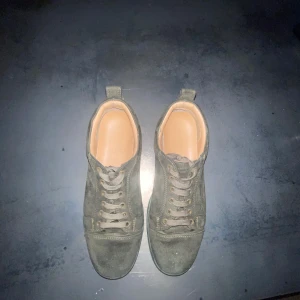 Gröna sneakers från Louboutin - Snygga gröna sneakers från Louboutin i mocka med klassisk röd sula. Skorna har snörning och en stilren design med märkets logga broderad på hälen. Perfekta för den som vill ha en touch av lyx i vardagen. Med nästan 8-10 i skick väldigt bra skick för att haft dem i 1 år har de varit andvända jag inkludera dustbag och låda med kvitto jag har dessutom en äktihets tag med allt
