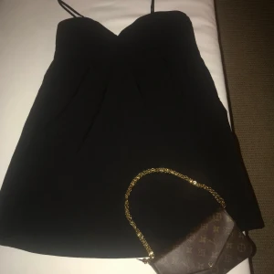 Svart axelbandslös klänning - Snygg svart axelbandslös klänning med en elegant och enkel design. Perfekt för en kväll ute eller en speciell tillställning. Klänningen har en smickrande passform och är lätt att matcha med olika accessoarer.