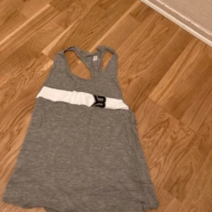 Nytt linne från Better Bodies stl S - Säljer en grå linnetopp från Better Bodies,  med en vit rand och svart logga på framsidan. Toppen har en brottarrygg och är perfekt för en avslappnad stil. Materialet är mjukt och bekvämt.Ny!!