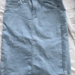 Ljusblå jeanskjol med slits - Snygg ljusblå jeanskjol med klassiska femficksdetaljer och en liten slits baktill. Perfekt för en avslappnad stil. Kjolen har en normal passform och är tillverkad i ett bekvämt denimtyg.