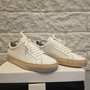 Vita sneakers från Givenchy - Snygga vita sneakers från Givenchy med en stilren design. Skorna har en vit ovandel i skinn och en beige sula. Givenchy-loggan syns på hälen och sulan. Perfekta för en minimalistisk look.