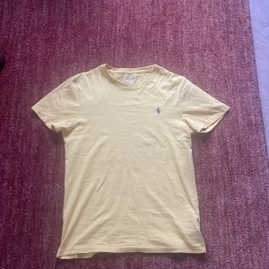 Gul t-shirt från Polo Ralph Lauren - Säljer en stilren gul t-shirt från Polo Ralph Lauren med en liten broderad logga på bröstet. T-shirten har en slim fit passform och är tillverkad i mjuk bomull. Perfekt för en avslappnad look! 