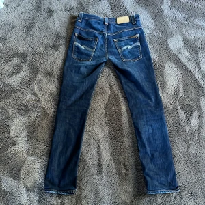 Blå jeans från Nudie  - Snygga blå jeans från Nudie Jeans med klassisk femficksdesign och kontrastsömmar. De har en normal passform och är perfekta för en avslappnad stil. Märkeslogga på insidan av linningen. Storlek 30/32 men men sitter lite tajtare.