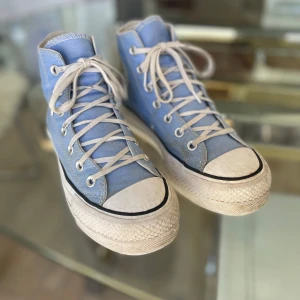 Blå höga sneakers från Converse All Star - Säljer ett par klassiska blå höga Converse All Star sneakers med vita snören och tåhätta. Skorna har den ikoniska loggan på sidan och en vit sula med svart rand. Perfekta för en avslappnad stil. Dom är i bra skick och har blivit andvända Max 10 gånger.