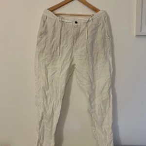 Vita linnebyxor med snörning - Snygga vita linnebyxor med avslappnad passform och snörning i midjan. Perfekta för varma dagar med sin lätta och luftiga känsla. Byxorna har fickor fram och bak för extra funktionalitet.