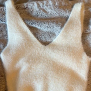 Vit ärmlös topp - Säljer en mysig vit ärmlös topp med djup v-ringning. Perfekt för lager-på-lager eller som den är. Toppen har en mjuk och fluffig textur som ger en unik känsla.