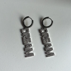 Säljer dessa DREAM örhängen” har tröttnat lite på dom”💓 - Snygga örhängen med texten 'DREAM' i glittrande silver. Perfekta för att ge en extra touch till din outfit. De hängande bokstäverna ger en cool och modern look.💞