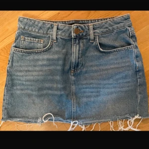 Jeanskjol med fransig kant - Snygg jeanskjol i klassisk blå denim med fransig kant och femficksdesign. Perfekt för en avslappnad stil. Kjolen har en knapp och dragkedja framtill.