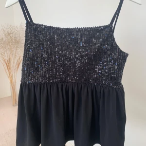 Svart paljettlinne från Gina Tricot - Säljer ett svart topp/blus från Gina Tricot med glittriga paljetter på överdelen och tunna axelband. Perfekt för en festlig look! ✨
