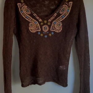 Brun tröja med pärldetaljer från Vanille - Säljer en brun tröja från Vanille med vackra pärldetaljer i olika färger runt halsringningen. Tröjan är tillverkad i en mjuk mohairblandning och har långa ärmar. Perfekt för att ge din outfit en unik touch! Gjord av alpacaull av mycket hög kvalitet.