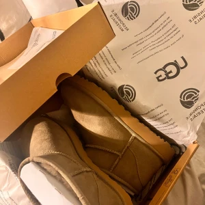 Beige boots från UGG Australia - Säljer ett par klassiska beige boots från UGG. De är tillverkade i mocka och har en rund tå. Perfekta för att hålla fötterna varma under kyliga dagar. Dom är en strlk 40 men passar 38-39