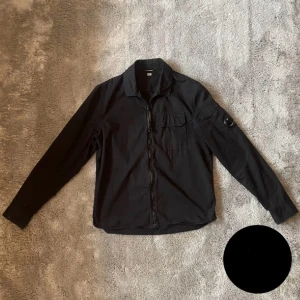 Svart overshirt från C.P Company - Snygg svart overshirt från C.P Company med dragkedja och en bröstficka. Perfekt till våren! Säljer då den satt för tajt för mig