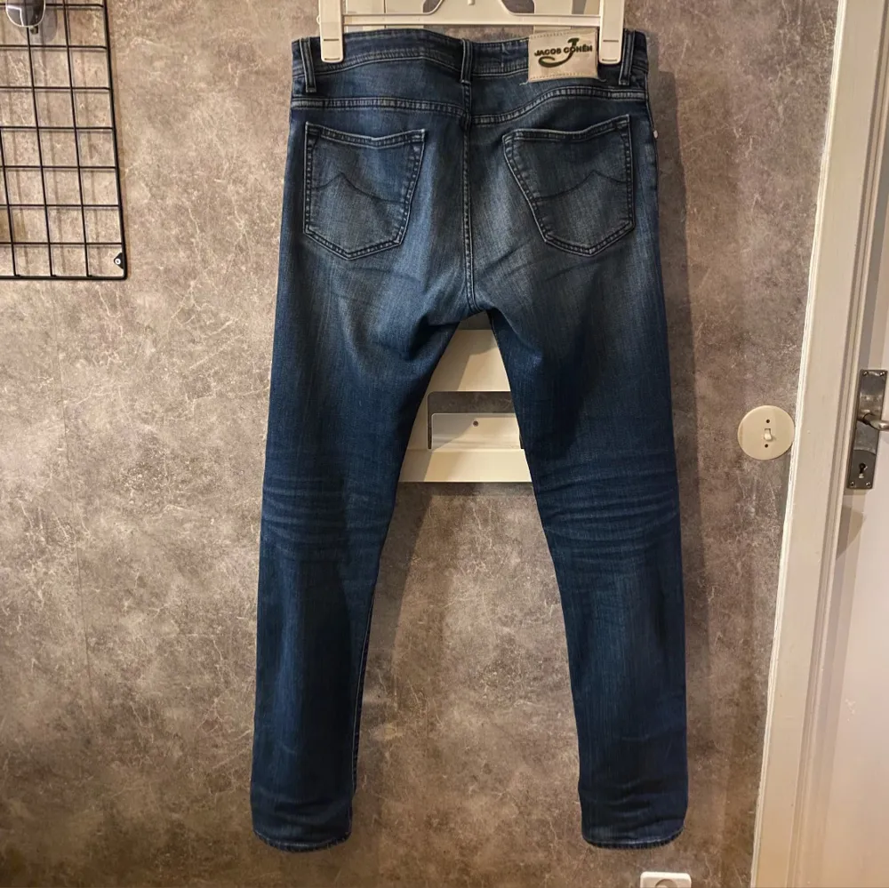 Snygga blå jeans från Jacob Cohen med knappgylf och klassisk femficksdesign. Jeansen har en stilren look med lätt slitna detaljer och en bekväm passform. Nypris 5000. Farkut & Housut.