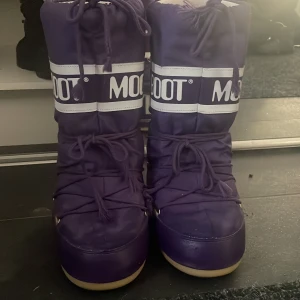 Lila Moon Boots - Säljer ett par lila Moon Boots,dem är äkta och enbart använda i ca 4 veckor,storleken är 39-41 och är perfekta efter en dag i backen med pjäxor,har en liten defekt på baksidan under skon,men ingent som påverkar skon utan håller värme ändå💗 Nypris 1400kr