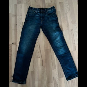 Blå jeans från Jack & Jones - Snygga blå jeans från Jack & Jones med en klassisk femficksdesign. De har en bekväm passform och är perfekta för en avslappnad stil. Jeansen har en knappgylf och bälteshällor. Mycket bra skick då dom i princip aldrig använts