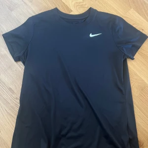 Svart t-shirt från Nike - Säljer en klassisk svart t-shirt från Nike med korta ärmar och den ikoniska loggan på bröstet. Perfekt för träning eller en avslappnad stil. Storlek M