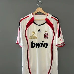 Vit och röd fotbollströja från Adidas - Säljer en vit fotbollströja från Adidas med röda och svarta detaljer. Tröjan har korta ärmar och ett tryck av Bwin på framsidan. Perfekt för fotbollsfans! Storlek M och en replika