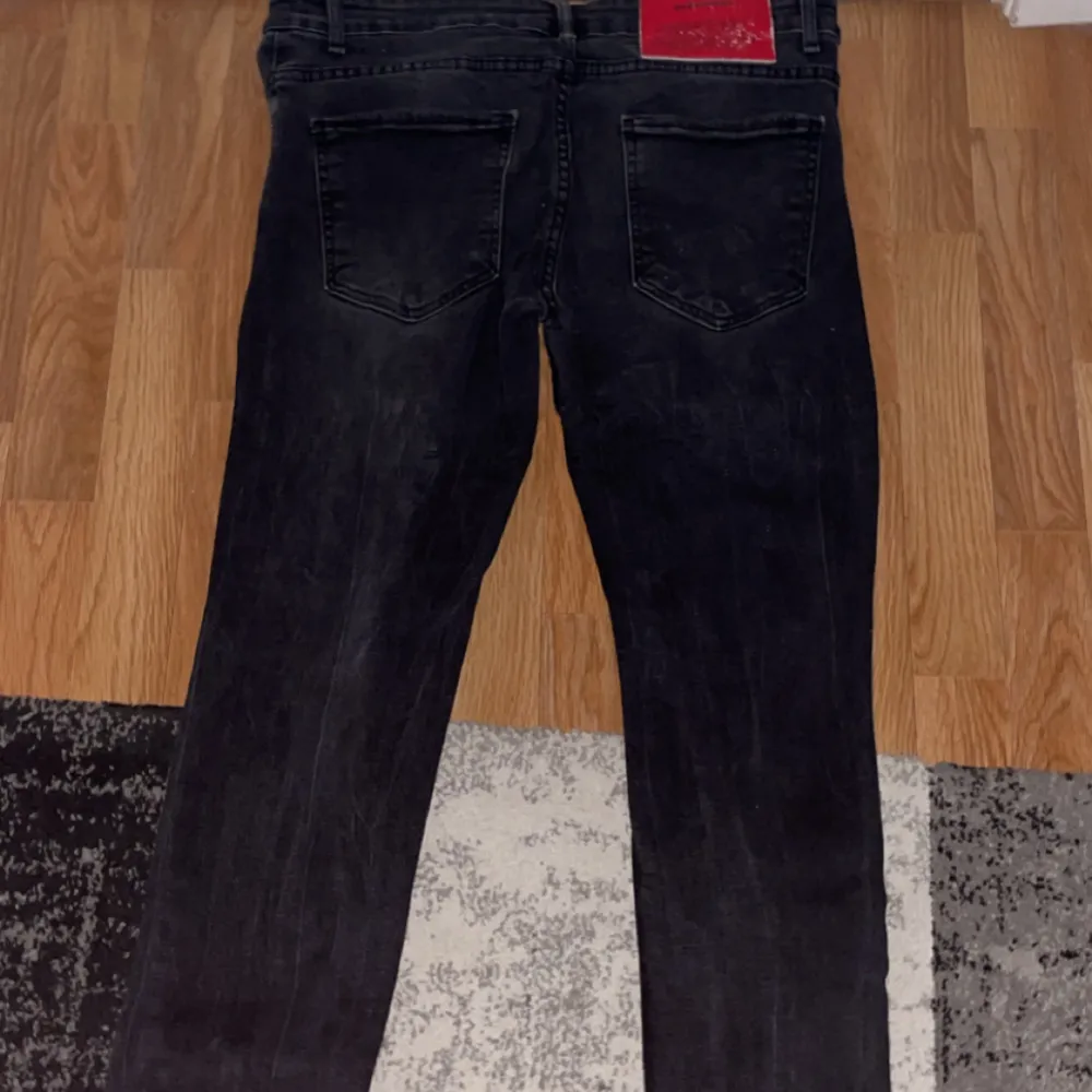 Snygga svarta jeans från Dsquared2 med slitna detaljer och knappgylf. Jeansen har en cool, distressed look med små färgstänk och en röd logotyp på baksidan. Perfekta för en trendig stil. Jeansen är slimfit och är använda några gånger. Jeansen är köpta på hemsidan disquared.. Farkut & Housut.