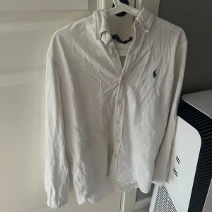 Vit skjorta från Ralph Lauren - Säljer en klassisk vit skjorta från Ralph Lauren med broderad logga på bröstet. Skjortan har långa ärmar och knappar framtill. Perfekt för en stilren look.