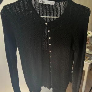 Svart kofta från Zara - Snygg svart kofta från Zara med ett diskret mönster och knappar framtill. Perfekt för lager-på-lager och att hålla sig varm under kyliga dagar.