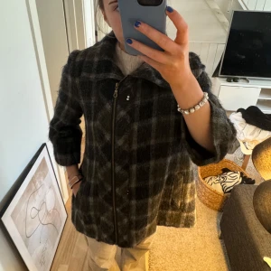 Grön rutig kappa - Säljer en stilren grå rutig kappa med dragkedja. Perfekt för kyligare dagar med sin långa ärm och klassiska design. Passar utmärkt för både höst och vinter. En tidlös investering för garderoben!