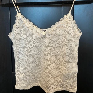 Vit spetslinne - Säljer ett vackert vitt spetslinne med smala axelband och blommigt mönster. v-ringad halslinje.