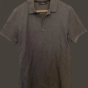 J.lindeberg - Snygg grå pikétröja från j.lindeberg med klassisk krage och knappar framtill. Perfekt för en stilren look. Passar till både jeans och chinos.