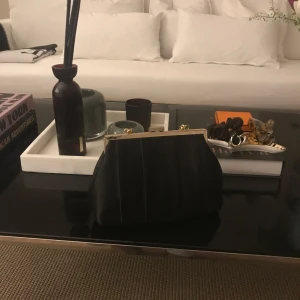  Clutch - Elegant svart kuvertväska med en stilren design. Väskan har en metallisk ram upptill som ger en lyxig touch. Perfekt för att komplettera en kvällsoutfit.