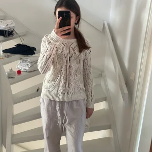 Vit stickad tröja - Säljer en vit stickad tröja med ett luftigt och öppet mönster. Tröjan har långa ärmar och en bred halsringning som ger en avslappnad look. Perfekt för lager-på-lager-stil eller sommarens svala kvällar.