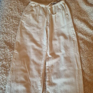 Vita linnebyxor från H&M - Snygga vita linnebyxor från H&M med elastisk midja och avslappnad passform. Perfekta för varma dagar med sitt lätta och luftiga material. Byxorna har praktiska fickor och en stilren design.