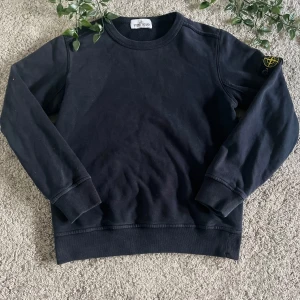 Svart sweatshirt från Stone Island - Snygg svart sweatshirt från Stone Island med rund hals och långa ärmar. Tröjan har en ikonisk logga på ärmen och ribbade muddar vid ärmslut och nederkant. Perfekt för en stilren outfit hela året. Den är ett fint skick och är barn storlek 142/10 år, jag säljer denna för att den är för liten och jag har ingen användning till den. Pris ej hugget i sten!