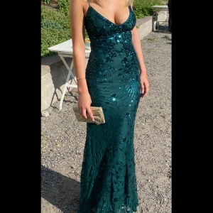 Balklänning - Snygg grön balklänning med paljetter och smala axelband. Klänningen har en öppen rygg med snörning och en figurnära passform. Jättsällsynt då den är köpt i USA Använd en gång för två år sen och är fortfarande så nöjd med den!! 