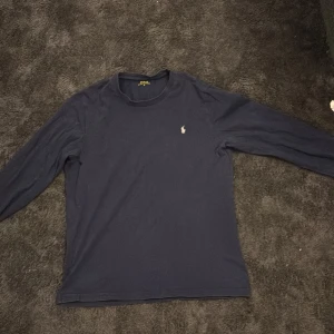 Mörkblå långärmad tröja från Polo Ralph Lauren - Säljer en stilren mörkblå långärmad tröja från Polo Ralph Lauren. Tröjan har en klassisk design med en liten broderad logotyp på bröstet. Perfekt för en avslappnad och snygg look.
