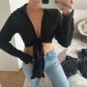 Svart knytblus - Snygg svart blus med knyt framtill. Blusen har långa ärmar och en djup v-ringning. 