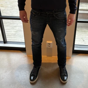 Mörkblå jag and Jones jeans - Snygga mörkblå jeans med en klassisk femficksdesign och lätt slitna detaljer. Byxorna har en slim passform och är perfekta för en avslappnad stil. De har en knappgylf och är tillverkade i ett robust denimtyg.