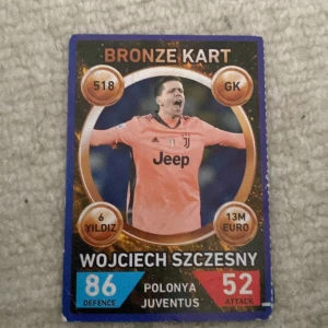 Fotbollskort Wojciech Szczesny Bronze Kart - Fotbollskort av Wojciech Szczesny i Juventus med bronstema. Kortet visar spelaren i en rosa tröja med Juventus-logga. Det har värden som 86 i försvar och 52 i attack. Perfekt för samlare av fotbollskort!