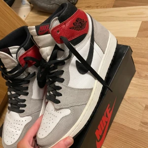 Air Jordan 1 retro high og - Säljer ett par Nike Air Jordans i en snygg kombination av grått, rött och vitt. Knappast använda och kan tänka mig gå ner i pris vid snabb affär!