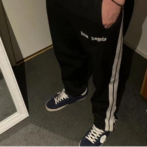 Svarta byxor från Palm Angels - Snygga svarta byxor från Palm Angels med vita ränder längs sidorna. Byxorna har en avslappnad passform Skriv för fler och bättre bilder 