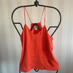 Röd linnetopp från H&M Conscious Collection - Säljer en snygg röd linnetopp från H&M Conscious Collection. Toppen har tunna axelband och en v-ringad design som ger en stilren look. Perfekt för varma sommardagar eller som ett lager under en kavaj.